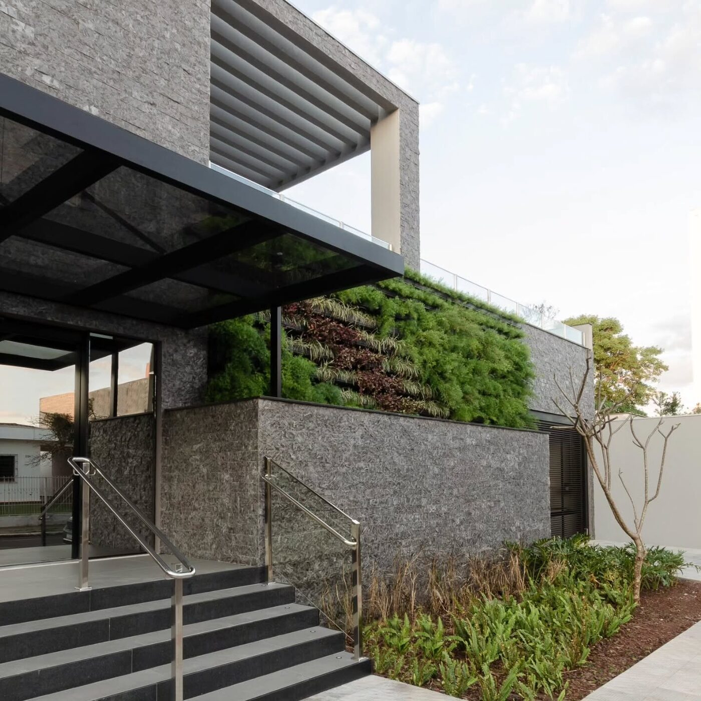 Fachada residencial com revestimento em pedra natural e jardim vertical